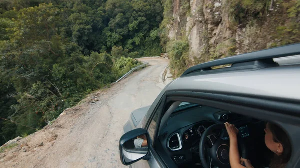 Dangerous road. Woman steers the car on a narrow road in mountains. Solo female traveler drives the car on a dangerous road near the edge