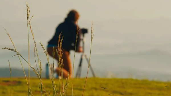 山上的摄影师 年轻的男性摄影师在日出时分 在青山上的三脚架上 用相机和心灵感应镜头拍照 免版税图库图片
