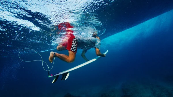 Surfer under the wave. Male surfer dives under the wave with surf board in the crystal clear tropical water
