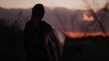 Sabah sörfü. Genç bir kadın sabahın erken saatlerinde sahilde sörf tahtasıyla yürüyor.