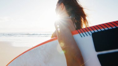 Kadın sörfçü, tropik plajda sörf tahtasıyla yürüyor.