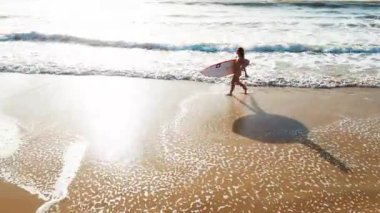 Seksi sörfçü havası. Bikinili genç sörfçü kadının kumlu mükemmel plajda sörf tahtasıyla yürüyüşünün havadan görüntüsü.