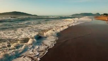 Kamera kumlu sahilde dalgalarla hızlı uçuyor. Brezilya, Florianopolis