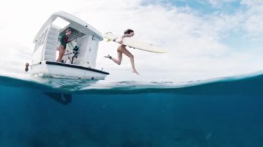 Kadın sörfçü bir tekneden okyanusa atlar.