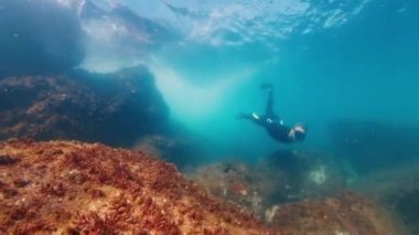 Serbest dalgıç bulanık denizde suyun altında yüzer ve kayalık dipte süzülür. Freediver okyanusun altında yüzüyor.