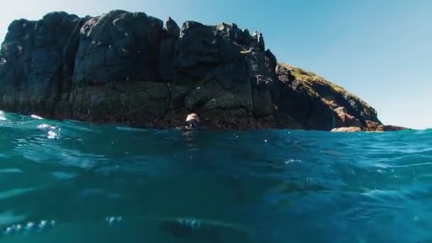 無料のダイバーは 濁った海で水中を泳ぎ 岩の多い島の近くに浮かぶ 岩の多い島の近くの海で自由に泳ぐ — ストック動画