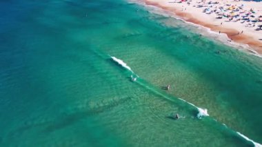 Yumuşak dalgalı deniz manzarası ve üzerinde insanların dinlendiği kumlu plaj. Brezilya 'nın Santa Catarina adasındaki Campeche plajı.