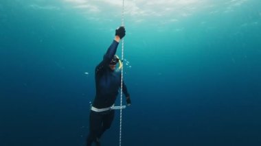 Freediver halatla çalışır ve yükselir. Kendine güvenen erkek serbest dalgıç, açık denizde ip boyunca ilerler ve derinlerden yükselir.