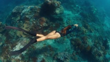 Resifte serbest kadın dalgıcı. Genç kadın serbest dalgıç su altında yüzer ve Endonezya, Bali 'deki Nusa Penida adasındaki sağlıklı mercan resiflerini keşfeder.