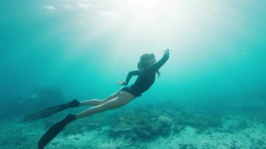 Serbest dalış yapan kadın suyun tadını çıkarıyor. Genç dişi serbest dalgıç suyun altında yüzer, döner ve suyun içinde olmaktan zevk alır.