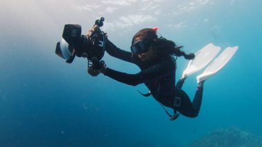 Hintli kadın sualtı fotoğrafçısı büyük su altı kamerasıyla yüzüyor. Denizde yüzen kameralı özgür bir kadın.