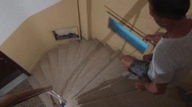 Adam eski konut binasının içindeki merdivenlerden aşağı koşuyor. Genç adam merdivenlerden aşağı koşuyor.