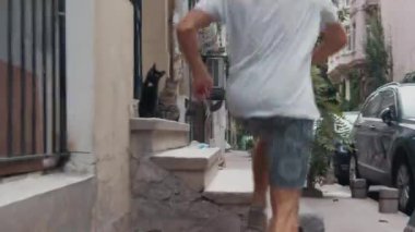 İSTANBUL, TURKEY - 8 Ağustos 2023: İstanbul 'un dar sokaklarında kafeler, kediler ve arabalar yol kenarına park edilmiş bir adam koşuyor