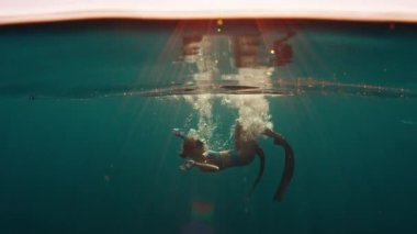 Serbest dalış yapan kadın gün batımında denizin altında yüzer ve rahatlar ve yüzeyin altında yüzer.