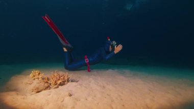 Freediver geceleri kumlu zeminde suyun altında yüzer.
