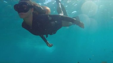 Genç bir kadın okyanusta yüzüyor. Dişi freediver su altında süzülüyor
