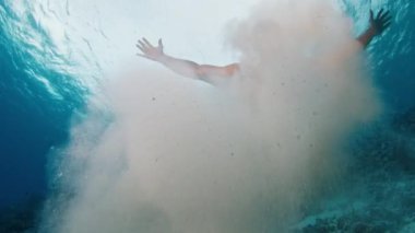 İnsan tropikal denizde su altında yüzer ve kumla oynar.