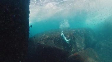 Freediver denizin altında yüzer ve kayanın yanına çıkar.