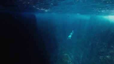 Freediver denizin altında yüzer ve kayanın yanına çıkar.