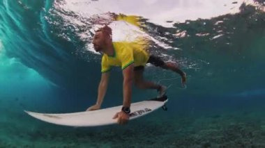 Sarı tişörtlü sörfçü Maldivler 'de sörf tahtasıyla dalganın altına dalıyor.