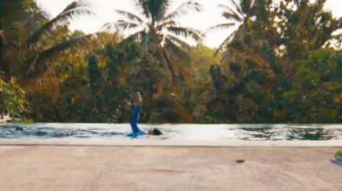 Arka planda palmiye ağaçları olan bir kadın havuzda yüzer.