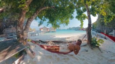 Genç adam plajdaki hamakta dinleniyor.