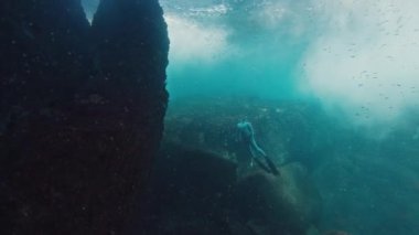 Freediver denizin altında yüzer ve kayanın yanına çıkar.