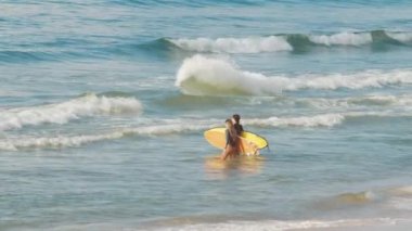 Güneş doğarken iki dişi sörfçü okyanusa girer.