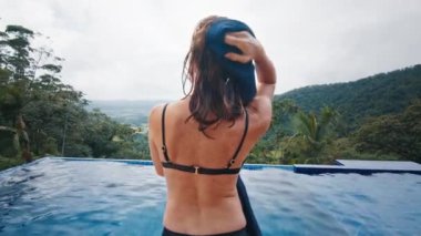 Kadın özel havuzun yanında durur ve kendini havluyla kurutur.