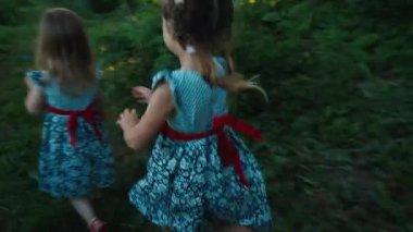Aynı elbiseyi giyen üç kız yaz bahçesinde koşuyor.