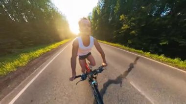 Genç adam gün batımında asfalt yolda bisiklet sürüyor.
