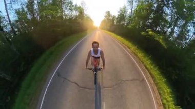 Genç adam gün batımında asfalt yolda bisiklet sürüyor.