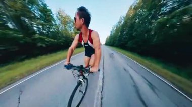 Bisiklet işi. Gün batımında asfalt yolda bisiklet süren genç bir adam.