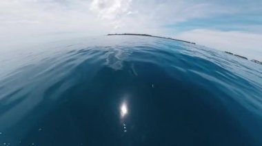 Tekne mavi denizde hareket ediyor. Kamera su yüzeyinden tekneye geçiyor.