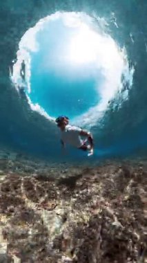 Maskeli adam okyanus dalgalarının altında dalıyor.