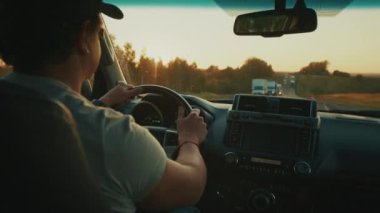 Gün batımında kamyonlarla dolu otoyolda ağır trafikte direksiyon sallayan kişi.