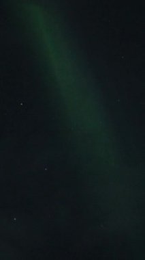 Aurora Borealis, doğal, gerçek hız görüntüsü. Gece gökyüzünde bazı bulutlar ve yıldızlarla kuzey ışıkları. Gökyüzünde bulutlarla şekillenen yeşil kuzey ışıklarının gürültülü bir görüntüsü.