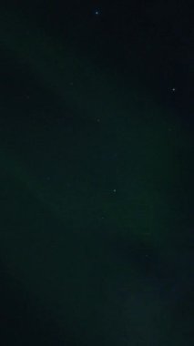 Aurora Borealis, doğal, gerçek hız görüntüsü. Gece gökyüzünde bazı bulutlar ve yıldızlarla kuzey ışıkları. Gökyüzünde bulutlarla şekillenen yeşil kuzey ışıklarının gürültülü bir görüntüsü.