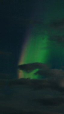 Aurora Borealis, doğal, gerçek hız görüntüsü. Gece gökyüzünde bazı bulutlar ve yıldızlarla kuzey ışıkları. Gökyüzünde bulutlarla şekillenen yeşil kuzey ışıklarının gürültülü bir görüntüsü.