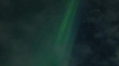 Aurora Borealis, doğal, gerçek hız görüntüsü. Gece gökyüzünde bazı bulutlar ve yıldızlarla kuzey ışıkları. Gökyüzünde bulutlarla şekillenen yeşil kuzey ışıklarının gürültülü bir görüntüsü.