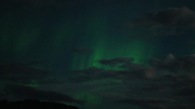Aurora Borealis, doğal, gerçek hız görüntüsü. Gece gökyüzünde bazı bulutlar ve yıldızlarla kuzey ışıkları. Gökyüzünde bulutlarla şekillenen yeşil kuzey ışıklarının gürültülü bir görüntüsü.