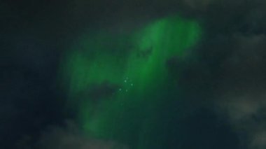 Aurora Borealis, doğal, gerçek hız görüntüsü. Gece gökyüzünde bazı bulutlar ve yıldızlarla kuzey ışıkları. Gökyüzünde bulutlarla şekillenen yeşil kuzey ışıklarının gürültülü bir görüntüsü.