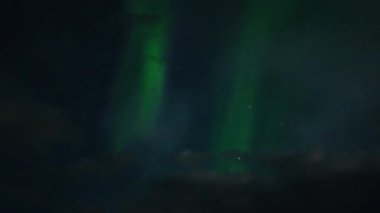 Aurora Borealis, doğal, gerçek hız görüntüsü. Gece gökyüzünde bazı bulutlar ve yıldızlarla kuzey ışıkları. Gökyüzünde bulutlarla şekillenen yeşil kuzey ışıklarının gürültülü bir görüntüsü.
