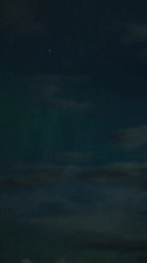 Aurora Borealis, doğal, gerçek hız görüntüsü. Gece gökyüzünde bazı bulutlar ve yıldızlarla kuzey ışıkları. Gökyüzünde bulutlarla şekillenen yeşil kuzey ışıklarının gürültülü bir görüntüsü.