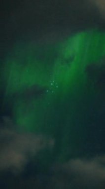 Aurora Borealis, doğal, gerçek hız görüntüsü. Gece gökyüzünde bazı bulutlar ve yıldızlarla kuzey ışıkları. Gökyüzünde bulutlarla şekillenen yeşil kuzey ışıklarının gürültülü bir görüntüsü.