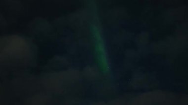 Aurora Borealis, doğal, gerçek hız görüntüsü. Gece gökyüzünde bazı bulutlar ve yıldızlarla kuzey ışıkları. Gökyüzünde bulutlarla şekillenen yeşil kuzey ışıklarının gürültülü bir görüntüsü.