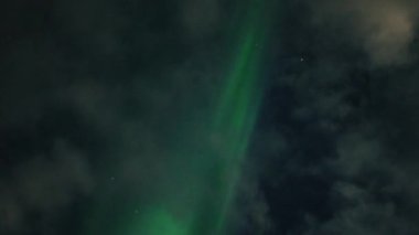 Aurora Borealis, doğal, gerçek hız görüntüsü. Gece gökyüzünde bazı bulutlar ve yıldızlarla kuzey ışıkları. Gökyüzünde bulutlarla şekillenen yeşil kuzey ışıklarının gürültülü bir görüntüsü.