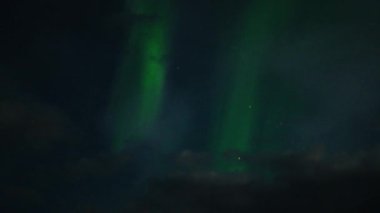 Aurora Borealis, doğal, gerçek hız görüntüsü. Gece gökyüzünde bazı bulutlar ve yıldızlarla kuzey ışıkları. Gökyüzünde bulutlarla şekillenen yeşil kuzey ışıklarının gürültülü bir görüntüsü.