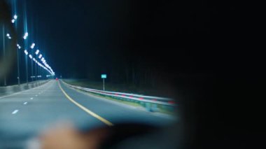 Gece yolculuğu. Aydınlatılmış boş otoyolda geceleyin direksiyon sallayan kişi. Sürücünün otobanda araba sürüşünün iç görüntüsü.