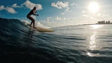 Dişi sörfçü gün batımında Maldivler 'de dalgalara biner ve çapraz adım atar.
